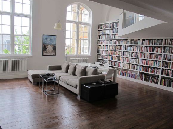 Loft apartment in a converted Victorian school with high ceilings, arched windows and a wall of books.