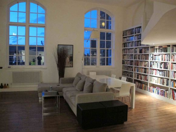 Loft apartment in a converted Victorian school with high ceilings, arched windows and a wall of books.