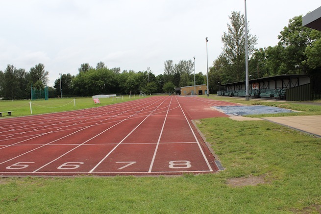 Athletics track surrounding various athletic setups with a playing field and tennis courts adjacent.