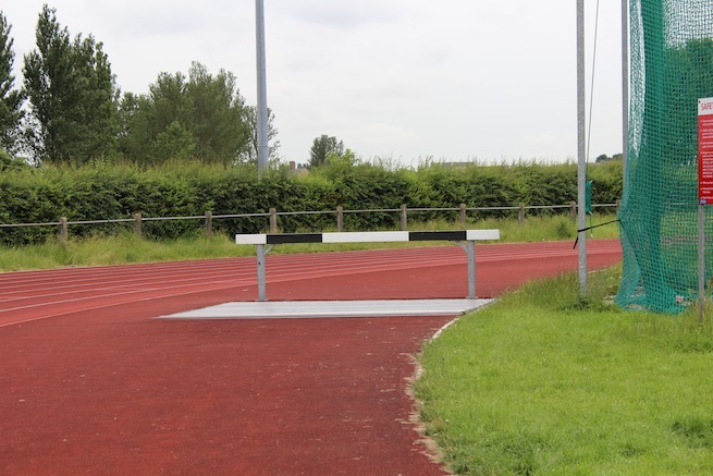 Athletics track surrounding various athletic setups with a playing field and tennis courts adjacent.
