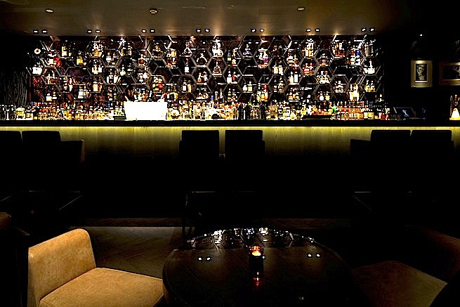 A stylish cocktail bar with glamorous surroundings. The bar boasts impressive storage cabinets and contemporary art work.