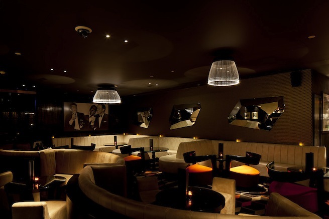 A stylish cocktail bar with glamorous surroundings. The bar boasts impressive storage cabinets and contemporary art work.