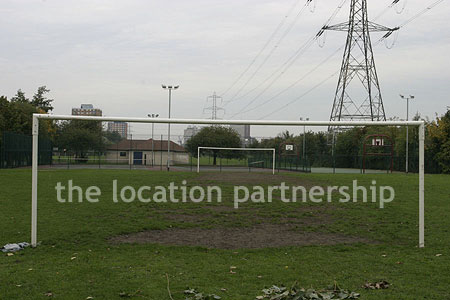 Small 5-a-side sized football pitch with urban backdrop of pylons and houses.