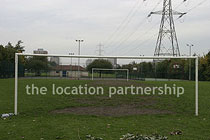Small 5-a-side sized football pitch with urban backdrop of pylons and houses.