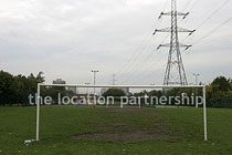 Small 5-a-side sized football pitch with urban backdrop of pylons and houses.