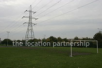 Small 5-a-side sized football pitch with urban backdrop of pylons and houses.