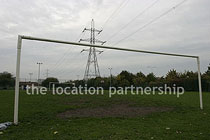 Small 5-a-side sized football pitch with urban backdrop of pylons and houses.