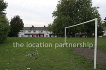 Small 5-a-side sized football pitch with urban backdrop of pylons and houses.
