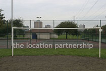 Small 5-a-side sized football pitch with urban backdrop of pylons and houses.