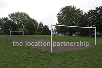 Small 5-a-side sized football pitch with urban backdrop of pylons and houses.