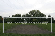 Small 5-a-side sized football pitch with urban backdrop of pylons and houses.