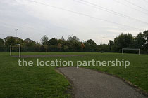 Small 5-a-side sized football pitch with urban backdrop of pylons and houses.