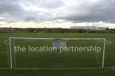 Football / cricket pitches with semi-urban backdrop and pavillion.