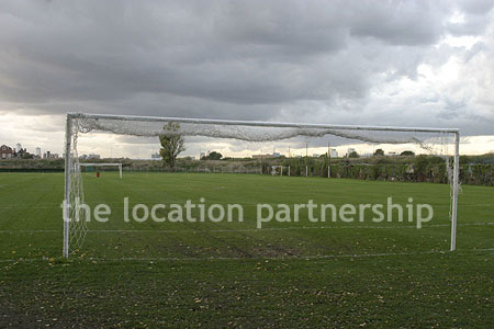 Football / cricket pitches with semi-urban backdrop and pavillion.