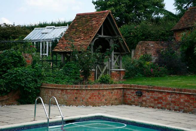 Characterful exterior and gardens of beautiful country house with treehouse, outbuildings, barns, swimming pool and tennis court.