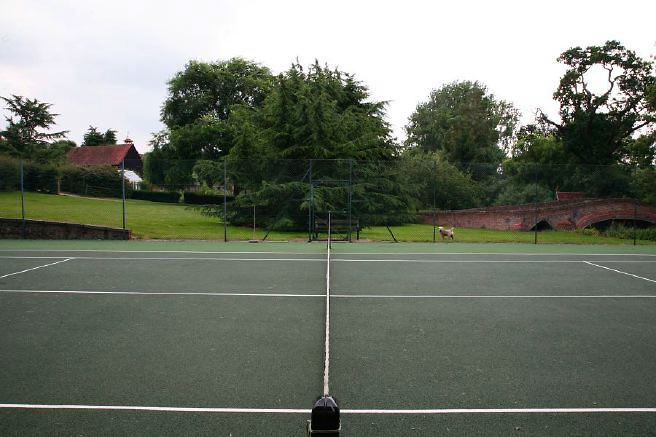 Characterful exterior and gardens of beautiful country house with treehouse, outbuildings, barns, swimming pool and tennis court.