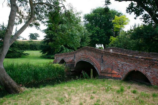 Characterful exterior and gardens of beautiful country house with treehouse, outbuildings, barns, swimming pool and tennis court.