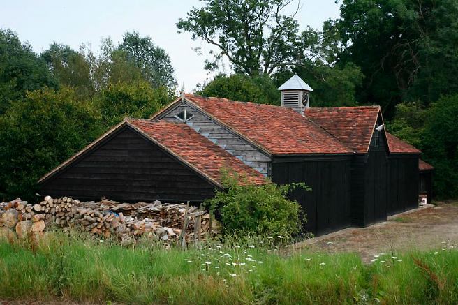 Characterful exterior and gardens of beautiful country house with treehouse, outbuildings, barns, swimming pool and tennis court.