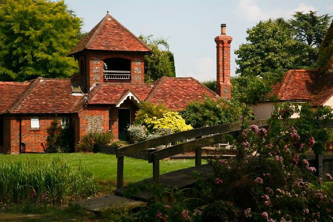 Characterful exterior and gardens of beautiful country house with treehouse, outbuildings, barns, swimming pool and tennis court.