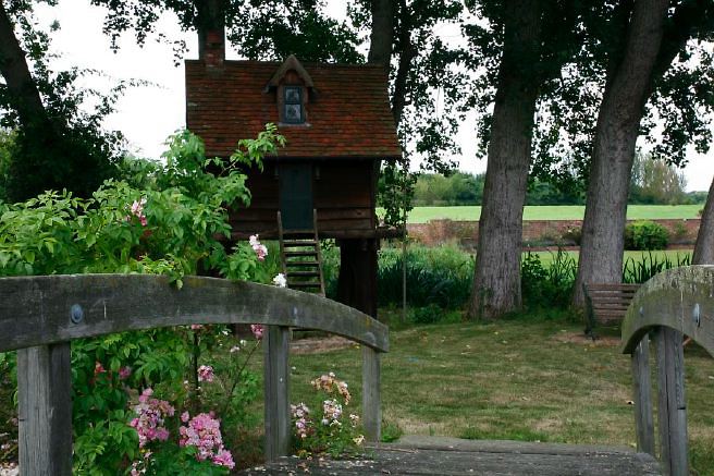Characterful exterior and gardens of beautiful country house with treehouse, outbuildings, barns, swimming pool and tennis court.