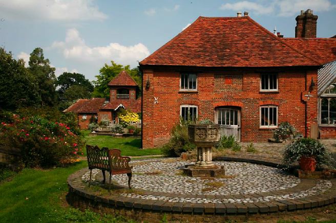 Characterful exterior and gardens of beautiful country house with treehouse, outbuildings, barns, swimming pool and tennis court.