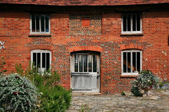 Characterful exterior and gardens of beautiful country house with treehouse, outbuildings, barns, swimming pool and tennis court.