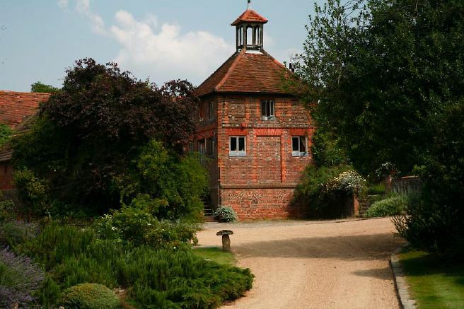 Characterful exterior and gardens of beautiful country house with treehouse, outbuildings, barns, swimming pool and tennis court.