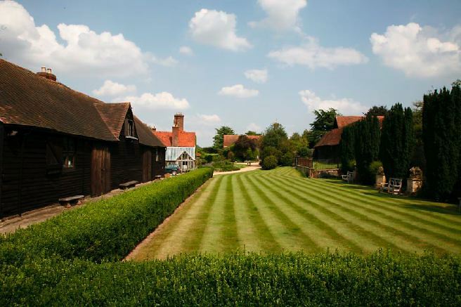 Characterful exterior and gardens of beautiful country house with treehouse, outbuildings, barns, swimming pool and tennis court.