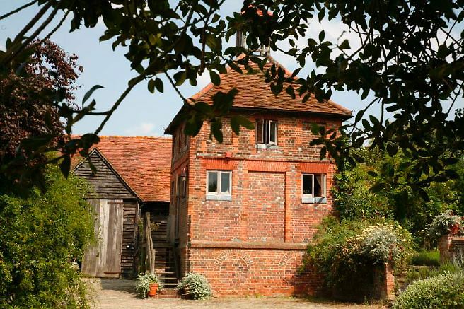 Characterful exterior and gardens of beautiful country house with treehouse, outbuildings, barns, swimming pool and tennis court.