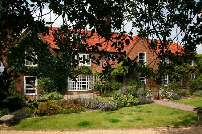 Characterful exterior and gardens of beautiful country house with treehouse, outbuildings, barns, swimming pool and tennis court.