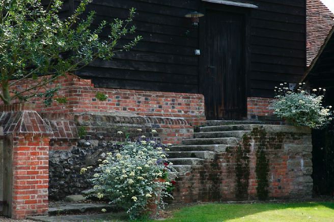 Characterful exterior and gardens of beautiful country house with treehouse, outbuildings, barns, swimming pool and tennis court.