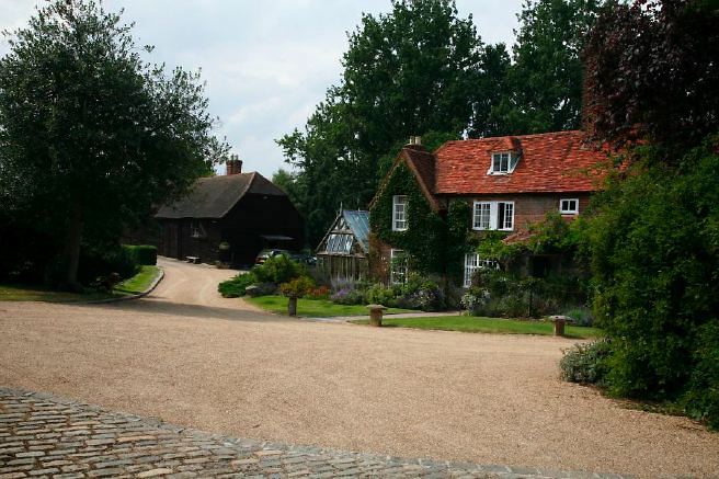 Characterful exterior and gardens of beautiful country house with treehouse, outbuildings, barns, swimming pool and tennis court.