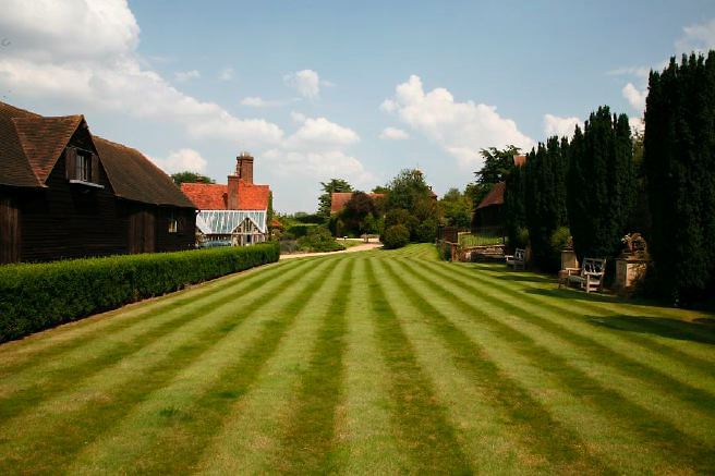 Characterful exterior and gardens of beautiful country house with treehouse, outbuildings, barns, swimming pool and tennis court.