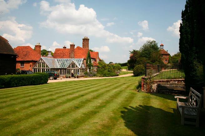 Characterful exterior and gardens of beautiful country house with treehouse, outbuildings, barns, swimming pool and tennis court.