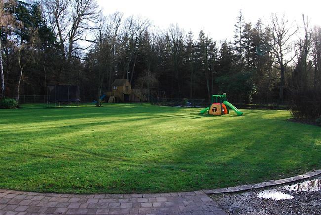 Country garden in woodland setting with a pond and children's play area.