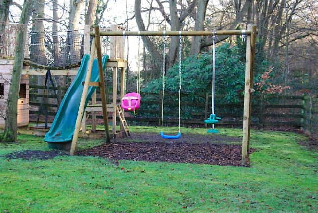 Country garden in woodland setting with a pond and children's play area.