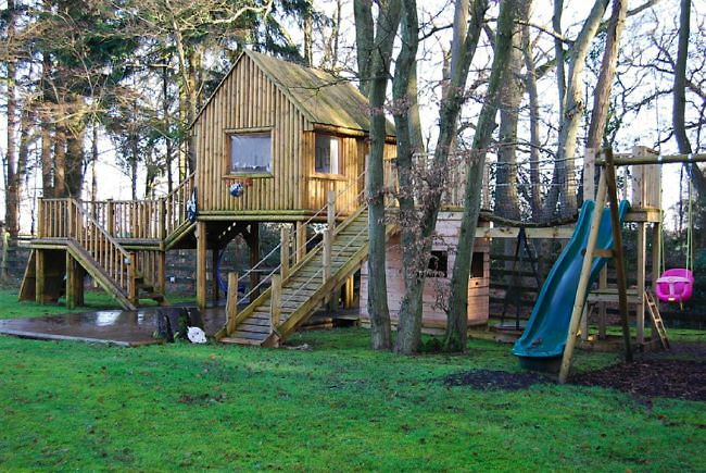 Country garden in woodland setting with a pond and children's play area.