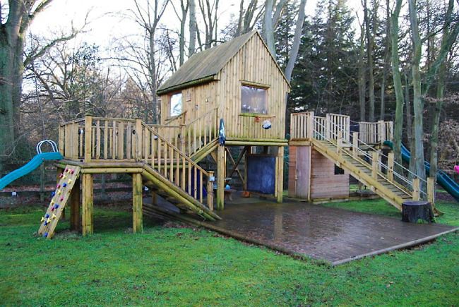 Country garden in woodland setting with a pond and children's play area.