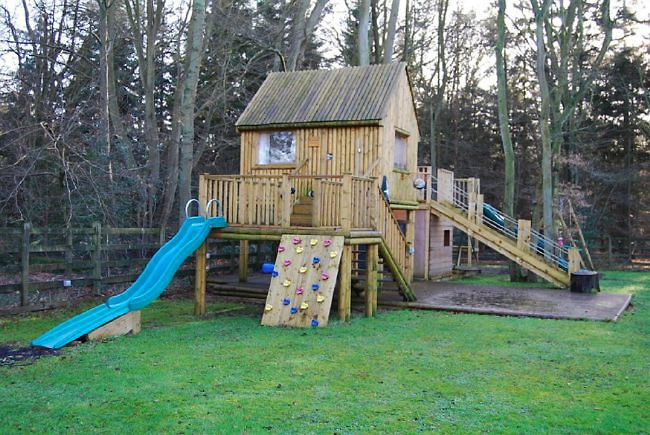 Country garden in woodland setting with a pond and children's play area.