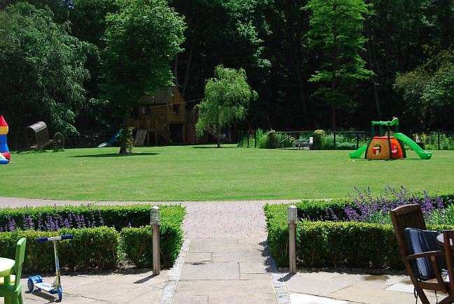 Country garden in woodland setting with a pond and children's play area.