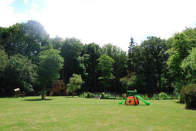 Country garden in woodland setting with a pond and children's play area.
