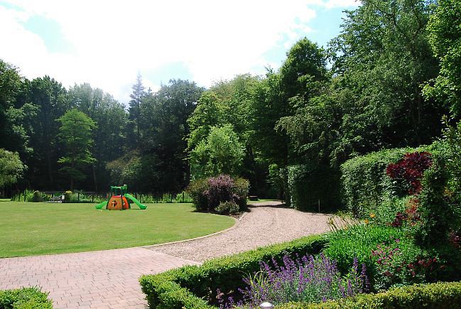 Country garden in woodland setting with a pond and children's play area.