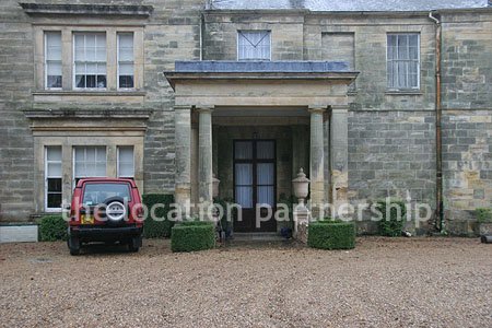 Gravel driveway leading to a pillared portico at the entrance to a large Country House