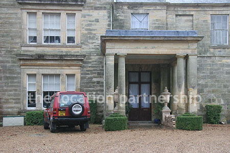 Gravel driveway leading to a pillared portico at the entrance to a large Country House