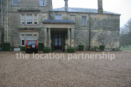 Gravel driveway leading to a pillared portico at the entrance to a large Country House