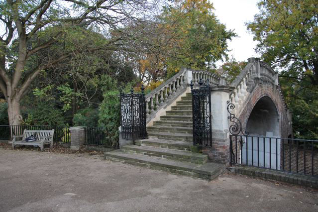 Beautiful historic house garden with an old stone bridge, walled gardens, manicured hedges, a circular pond and an ornate fountain