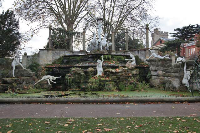 Beautiful historic house garden with an old stone bridge, walled gardens, manicured hedges, a circular pond and an ornate fountain