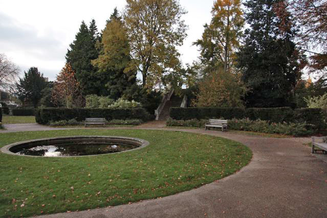 Beautiful historic house garden with an old stone bridge, walled gardens, manicured hedges, a circular pond and an ornate fountain