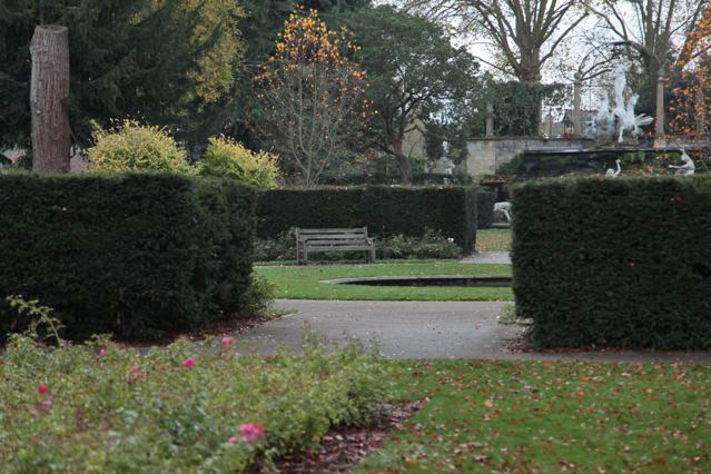 Beautiful historic house garden with an old stone bridge, walled gardens, manicured hedges, a circular pond and an ornate fountain