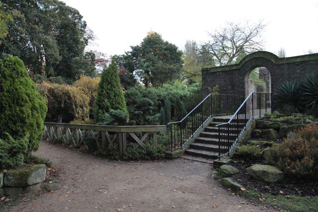 Beautiful historic house garden with an old stone bridge, walled gardens, manicured hedges, a circular pond and an ornate fountain